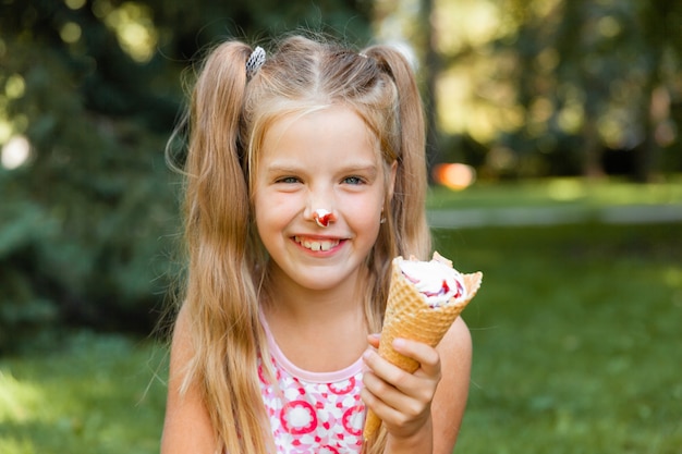 公園で夏にアイスクリームを食べる美しい小さなブロンドの女の子 アイスクリームと陽気な女の子 プレミアム写真