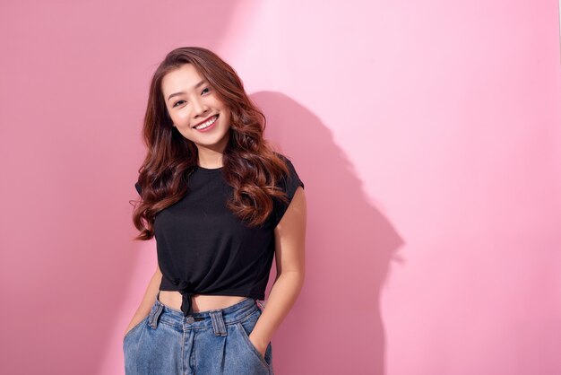 Chân dung xinh đẹp Cô gái trẻ vui vẻ Châu Á tạo dáng trong trang phục giản dị với nụ cười rạng rỡ đứng cách biệt trên bức tường màu hồng Ảnh cao cấp
