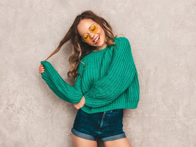Beautiful sexy smiling gorgeous girl in green trendy sweater. woman posing in round sunglasses. model having fun and showing her tongue Free Photo