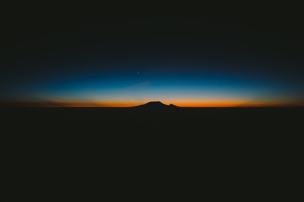Beautiful shot of dark hills with the amazing orange and blue sunset on the horizon Free Photo