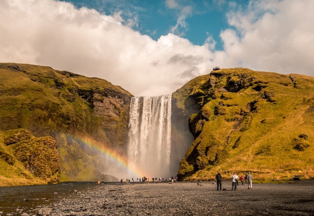 アイスランドのスコゥガフォスの側に虹のある滝の近くに立っている人々の美しいショット 無料の写真