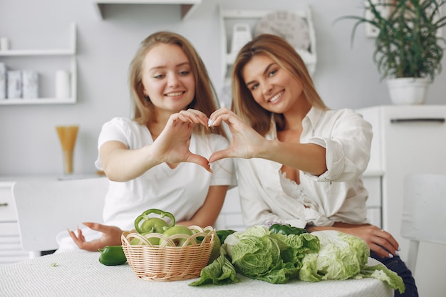 Beautiful and sporty women in a kitchen with vegetables Free Photo