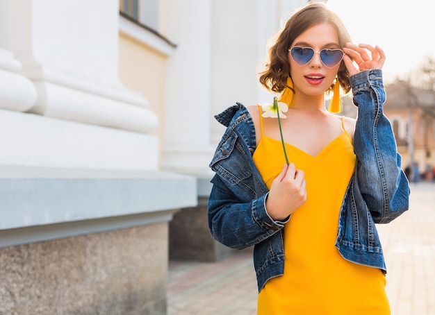 美しいスタイリッシュな流行に敏感な女性のポーズ ストリートファッション 花を持って 黄色のドレス デニムジャケット 自由奔放に生きるスタイル 春夏の ファッショントレンド 笑顔 流行の青いサングラス 笑顔 晴れ 無料の写真