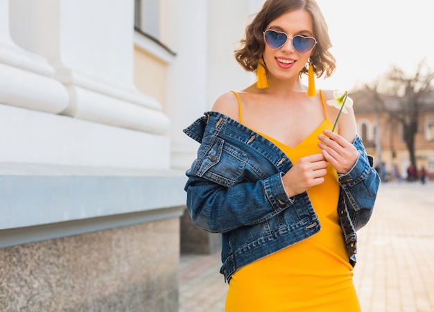 美しいスタイリッシュな流行に敏感な女性のポーズ ストリートファッション 花を持って 黄色のドレス デニムジャケット 自由奔放に生きるスタイル 春夏の ファッショントレンド 笑顔 流行の青いサングラス 笑顔 晴れ 無料の写真