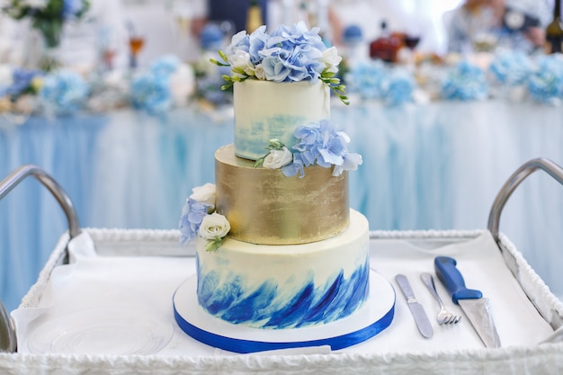 トレイに花で飾られた美しいウェディングケーキをクローズアップ フォークとナイフで白と青の階層型ウェディングケーキ プレミアム写真