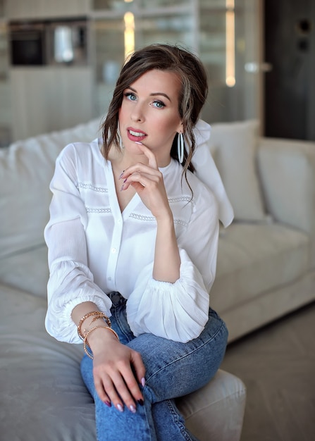 Premium Photo Beautiful Woman In Blue Jeans And A White Shirt Is Sitting On The Sofa Portrait Of A Young Woman