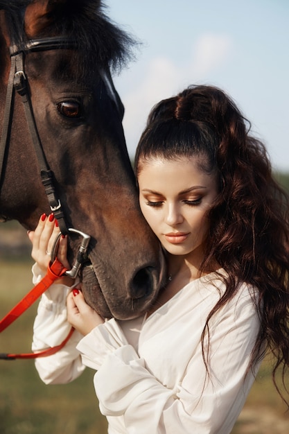 美しい女性は馬をなでるとフィールドで手綱を保持 プレミアム写真
