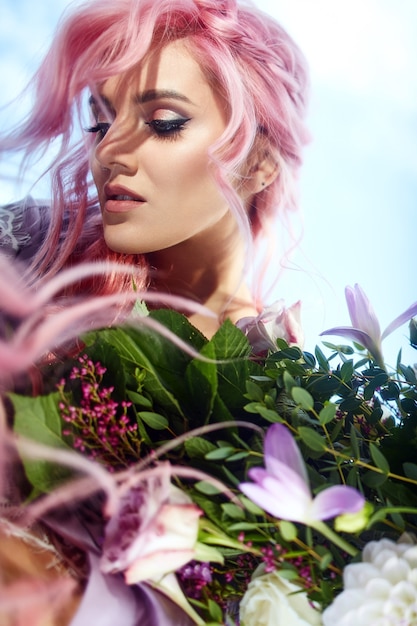 Beautiful woman with pink hair holds large bouquet with greenery and violet flowers Free Photo