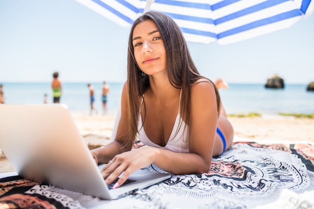 EARN $200, $300, $500 PER DAY 10,000 PER MONTH ON AUTOPILOT Beautiful-woman-working-online-laptop-while-lying-beach-sun-umbrella-near-sea-happy-smiling-freelancer-girl-relaxing-using-notebook-freelance-internet-work_231208-5329