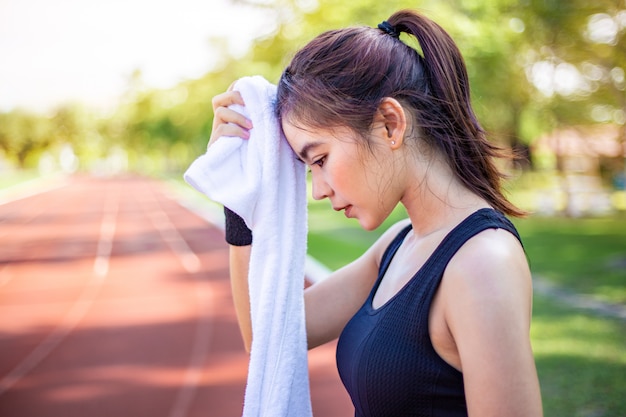 Beautiful young asian woman wiping off her sweat after her morning exercise at a running track Premium Photo