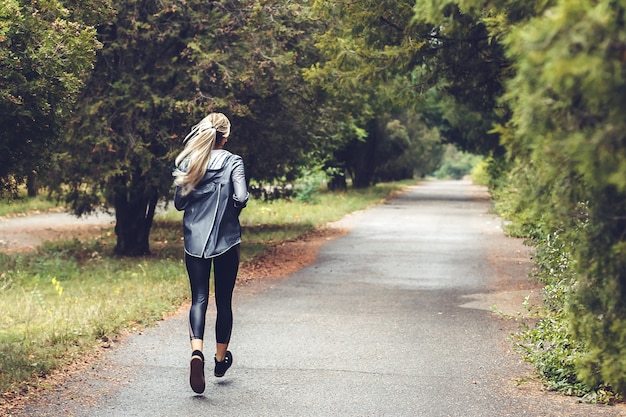 Beautiful young blonde girl with long hair is running in a park at ...