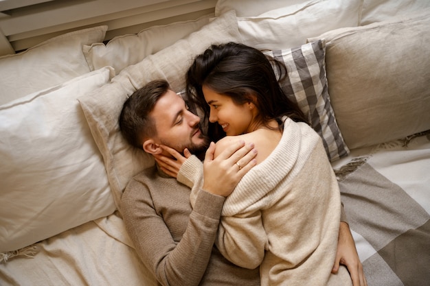 Beautiful young happy couple relaxing in bed and smiling, embracing Free Photo
