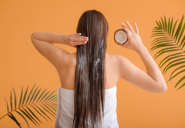 Beautiful young woman applying coconut oil on her hair against color Premium Photo