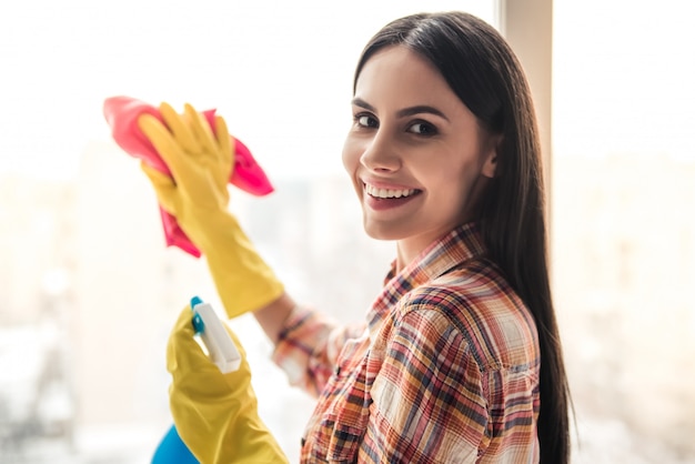 Premium Photo | Beautiful young woman is smiling while cleaning window.