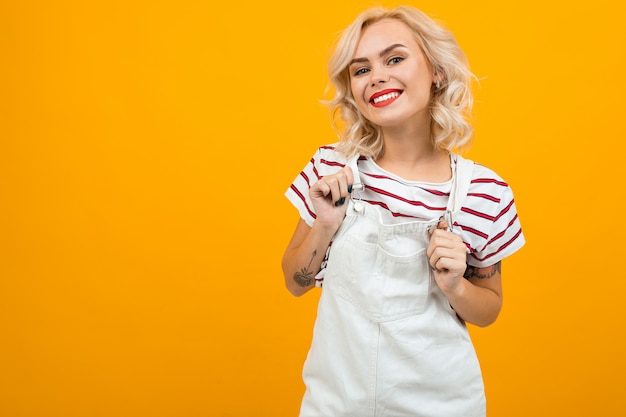 Premium Photo Beautiful Young Woman With Short Blonde Curly Hair And Bright Makeup In White Overalls Gesticulated And Smiles Portrait Isolated On Orange