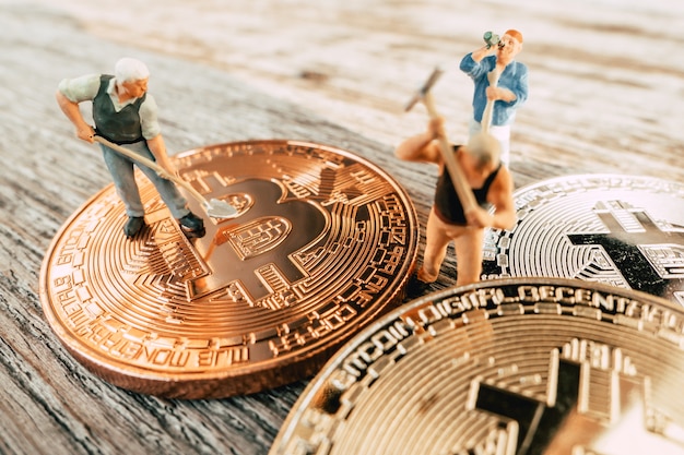 Bitcoin mining miniature people digging on valuable coin wood background Premium Photo