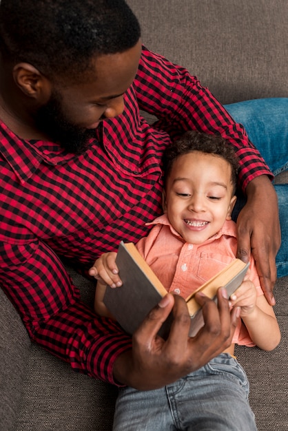 黒人の父とかわいい息子がソファで本を読んで 無料の写真
