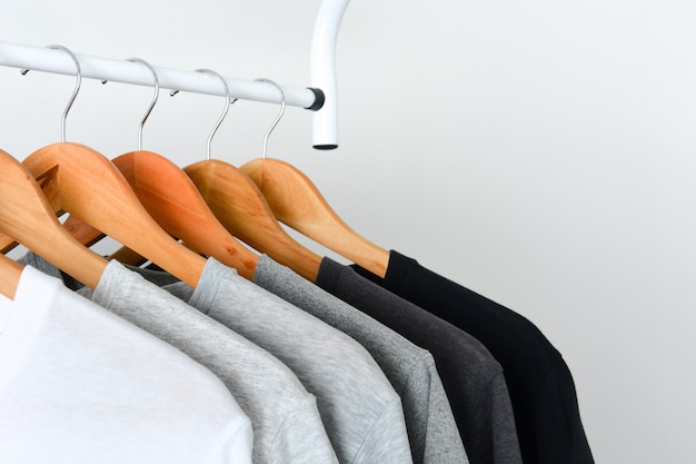 Black, gray and white color t-shirt hanging on wooden clothes hanger ...