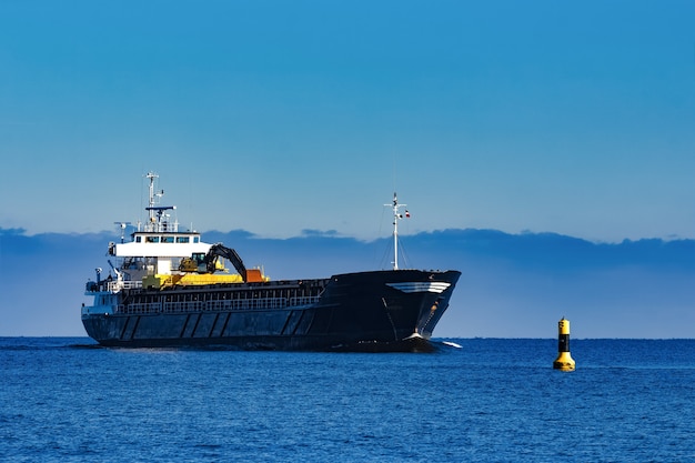 ブラックセーリングバルクキャリア 海沿いの晴れた日に静水中を移動するロングリーチショベルを搭載した貨物船 プレミアム写真