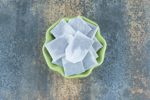 Black teabags in green bowl on marble. Free Photo