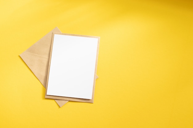 Blank white card with kraft brown paper envelope template mock up on yellow background Premium Photo