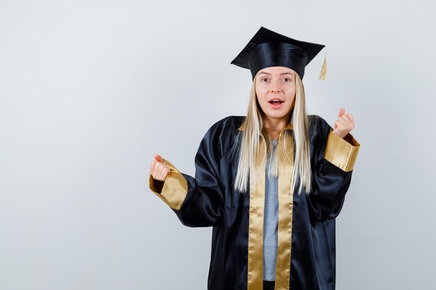 Free Photo | Blonde girl in graduation gown and cap showing winner ...