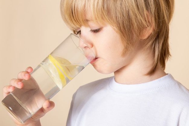 Free Photo | Blonde kid little cute drinking lemon juice on pink wall