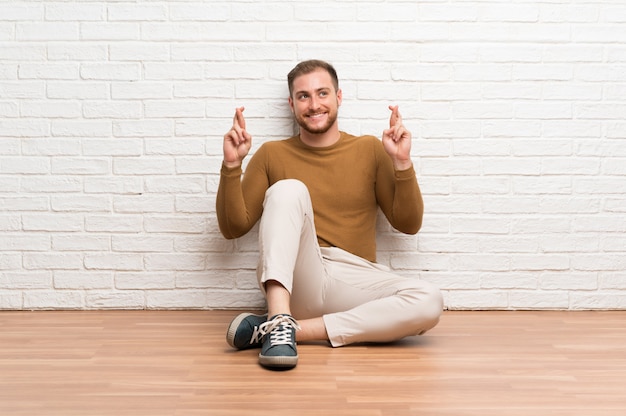 Premium Photo Blonde Man Sitting On The Floor With Fingers Crossing
