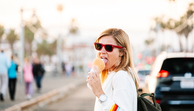A Blonde Woman In Glasses Enjoys Ice Cream At Sunset O