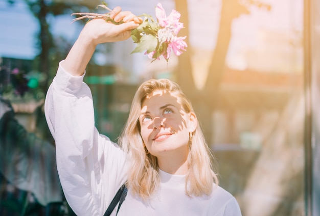 Blonde young woman holding flowers in hand shielding her eyes from the sunlight Free Photo