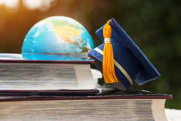 Blue graduation cap on opening textbook with blur of america earth world globe model map in library room of campus Premium Photo