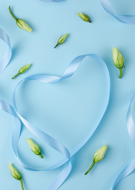 Blue ribbon in a heart shape with flower buds. Premium Photo