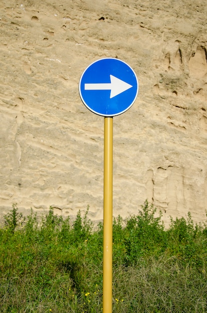 風化した古代の壁に矢印の付いた青い道路標識 プレミアム写真