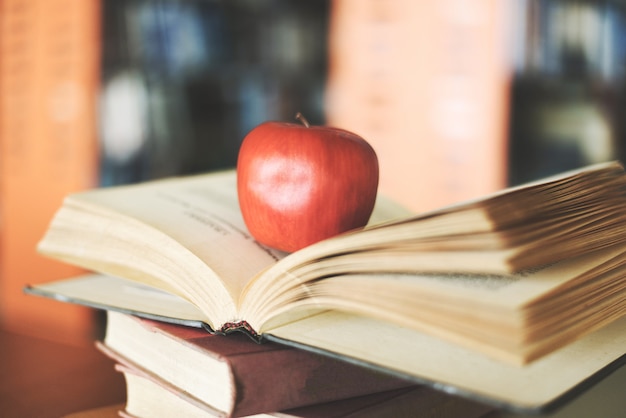 図書館のテーブルの上の本 木製の机の上の古い本のスタックを学習し 開いた本 学校概念に戻ってアップルとぼやけた本棚部屋の背景 プレミアム写真