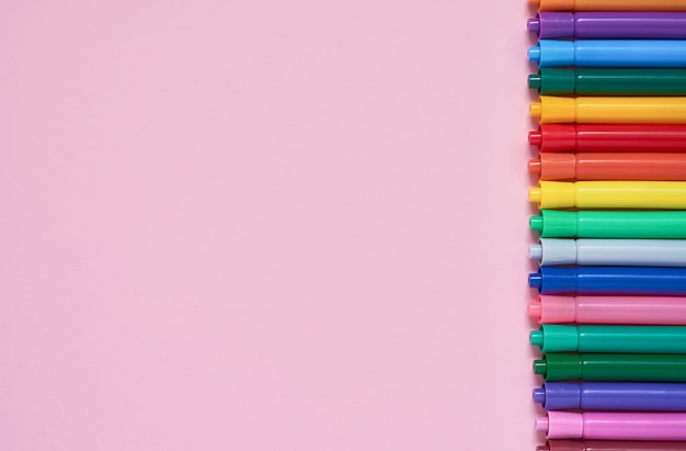 Border of colored felt tip pens on pink background with copyspace Premium Photo