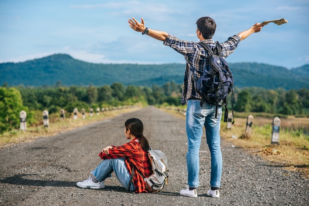 Both male tourists stand and raise their hands on both sides. female tourists sitting on the street Free Photo