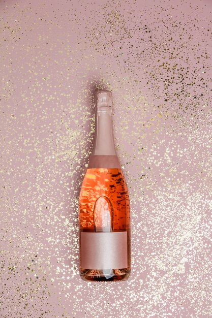 ゴールドのラメ入りピンクの背景 トップビューでシャンパンのボトル プレミアム写真