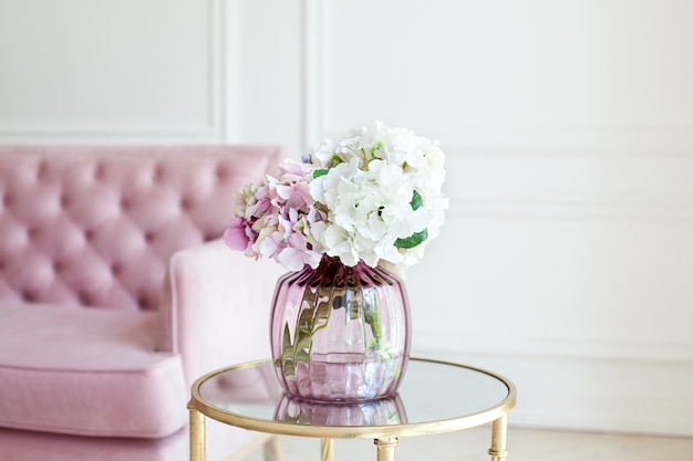 ガラスの花瓶にパステル調のアジサイの花束 自宅の花瓶の花 紫陽花の美しい花束は 白いリビングルームのピンクのソファの近くのテーブルの上の花瓶にあります ホームインテリア スカンジナビア プレミアム写真