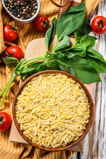 Premium Photo | A bowl of raw orzo pasta with basil leaves, tomatoes ...