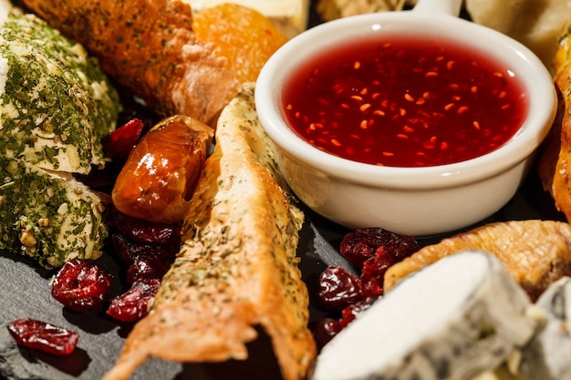 Bowl with cranberry sauce stands between pieces of cheese on black plate Free Photo