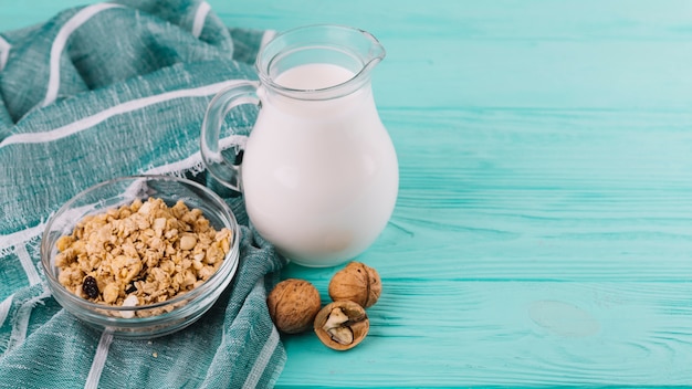 Bowls of cereals; milk jar and walnuts on green wooden table with cloth