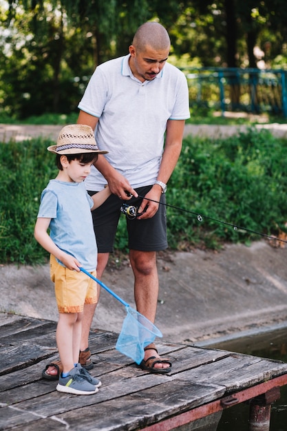 Boy holding fishing net standing with his father on pier Free Photo