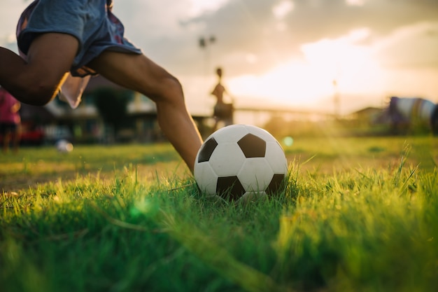緑の芝生のフィールドでストリートサッカーサッカーをしながら裸足でボールを蹴る少年 プレミアム写真