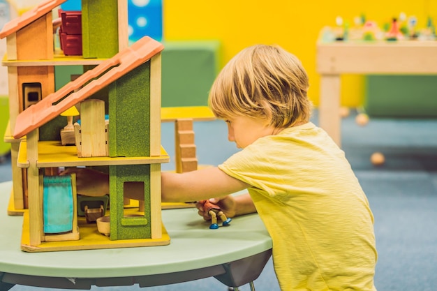 Premium Photo | Boy playing with wooden house in kindergarten.