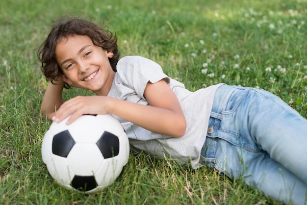 サッカーボールを持つ草に座っている少年 無料の写真