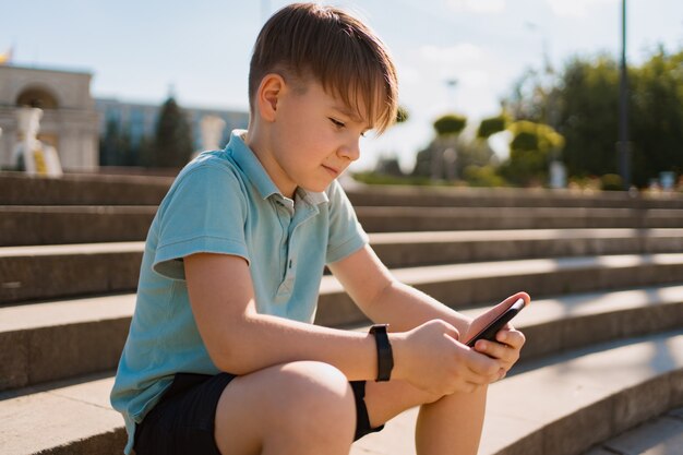 スマートフォンを手にして階段に座っている少年と面白い動画を見て緑のペニーボード 無料の写真