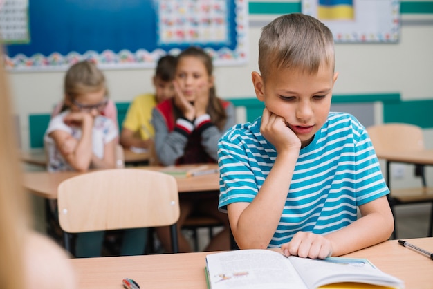 Boy Sitting At School Desk Reading Free Photo