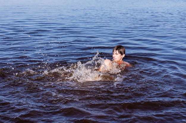 川 海 または湖の波状の青い水で泳いで水しぶきの少年 プレミアム写真