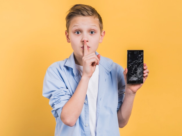 Lips Against The Glass.Free Photo A Boy With Finger On Lips Showing Broken Smartphone Glass Standing Against Yellow Background