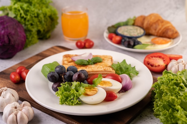 Breakfast consists of bread, boiled eggs, black grape salad dressing, tomatoes, and sliced ââonions. Free Photo